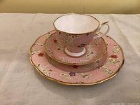 Plate, cup, and saucer stacked showing pink floral blush pattern and gold scalloped edging