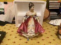 Front view of Royal Doulton Southern Belle porcelain figurine in original styrofoam packaging, showing detailed dress and figure features.