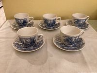 Five Wedgwood Countryside tea cups placed on their matching saucers, arranged on a flat surface showing the blue and white pastoral pattern on porcelain.