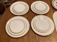 Four stacks of plates on a wooden table showing different sizes of plates with gold rim detail.