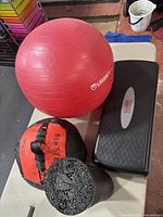 Overview of the fitness items: red exercise ball, weighted ball, aerobic step, and foam roller on a table