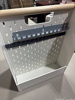 Front and inner view of the white metal gardening tool organizer showing the perforated panel, black metal rack, and wooden handle.