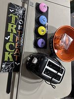 Overview photo showing Halloween yard sign, dog training buttons, black toaster, orange bowl with lights