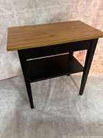 Front angled view of wooden end table showing natural pine wood top with black painted legs and lower shelf.