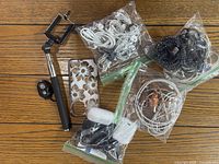 Photo showing various phone accessories including selfie stick, earbuds, iPhone cases, and cords in plastic bags laid out on wooden surface.