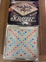 Photo of deluxe Scrabble board on table with box lid showing a hand rotating the board.