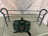 Photo displaying gray plastic shoe rack with metal rods behind a green Kodiak waist bag with zippered pockets and beverage holder.