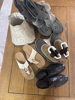 Overview of all footwear items and lampshades on wooden floor: black patent shoes, Eddie Bauer fur-lined boots, Manitoba mukluk boots, beige sandals, two lampshades.