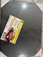 Set of six black slate plates, sealed in packaging with product label showing dimensions 12x15.75 inches and description "Slate Plate". Plates placed on concrete floor.