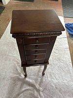 Closed view of dark brown wooden standing jewellery box showing five drawers and carved details.