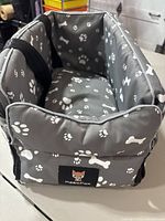 Grey dog carrier with white paw and bone patterns, showing padded interior and MagicFox logo on front.