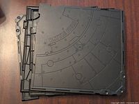 Stacked black plastic Bakugan stadium playset base pieces, showing embossed Battle Brawlers text and circular detail pattern.