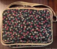 Front view of the black fabric organizer bag patterned with red, white, beige circles and beige trim and strap.