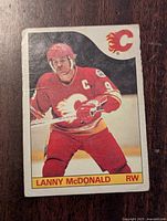 Front of the 1985-86 O-Pee-Chee hockey card showing Lanny McDonald in Calgary Flames uniform, mid-action pose with Flames logo at top right and name/title below.