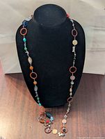 Front view of the long multicolour necklace displayed on a black bust, showing the colorful bead composition and circular resin pieces.