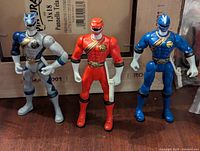 Front view of the three Wild Force Power Rangers action figures in red, blue, and silver standing upright on a wooden surface.