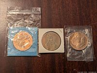 Three Franklin Mint bronze coins packaged individually, showing the front portraits of Alexander Mackenzie, Earl of Selkirk, Louis Fontaine and Robert Baldwin. Positioned on a wooden surface.