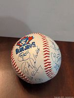Baseball showing large Blue Jays logo and multiple facsimile player signatures on white surface with red stitching.