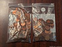Two clear resealable bags of pennies laid flat on a wooden surface, showing coins inside the bags.