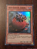Front view of a Yu-Gi-Oh Red-Eyes Black Chick 1st Edition holographic card showing illustration, stats, and text.