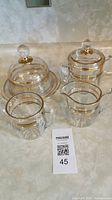 Photo of the glassware set showing butter dish with dome lid, sugar bowl, creamer, and spooner all with gold bands and clear glass handles.