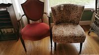 Pair of two chairs: pink velvet wooden armchair and embroidered fabric armless chair, shown on hardwood floor near window with natural light.