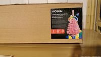 Box packaging for a NOMA 7-inch color-changing pink tabletop Christmas tree with LED lights and timer features.