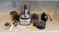 Photo showing all items in the lot on countertop including Cuisinart food processor, Black & Decker hand blender, rolling pin, ladle, flour sifter, peeler, and other kitchen tools and accessories.
