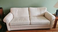 Front view of one cream-coloured loveseat showing cushioned seat and back with two cushions each, fabric upholstery, and rolled arms.