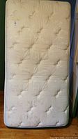 Single mattress front side showing white quilted fabric surface and tufted button design, slight discoloration marks on surface