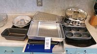 All baking pans, muffin pans, cooling rack, and bundt pans arranged on a countertop showing variety and condition