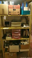 Full view of metal shelves with various office supplies including binders, a digital clock, phone, and storage containers.