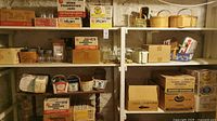 Shelving unit with multiple cardboard boxes of preserving and jelly jars from various brands; wooden baskets on top shelf