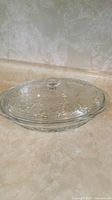 Clear glass serving dish with lid photographed on beige counter.