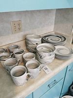 Full set of black and white swirl patterned dinnerware including large plates, small plates, bowls, and mugs arranged on countertop.