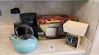 Lot arranged on kitchen counter: boxed 2-slice toaster, blue kettle, white mechanical kitchen scale, Hamilton Beach blender, Black & Decker coffee maker