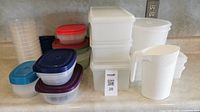 Multiple assorted tupperware containers of varying sizes and colors, including a white pitcher, displayed on kitchen countertop.