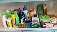 Overview of assorted cleaning supplies, including detergent bottles, spray bottles, boxes of wipes, microfiber cloths, and scrubbing pads.