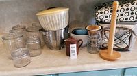 Glass canisters, salad spinner, colander, small ceramic honey jar, glass pour-over with ceramic dripper, wooden paper towel holder, insulated coolers in background