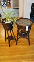 Two dark brown wicker planters; one with a round glass top and a plant inside, the other with a lower shelf holding a ceramic pot.