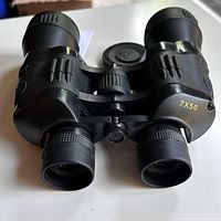 Front view showing the eyepieces, focus knob, and attached rubber lens caps. Embossed star and silhouette designs visible on the body. 7x50 marking on the right barrel.