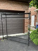 Full view of the black steel freestanding garment rack showing its size and structure outdoors.
