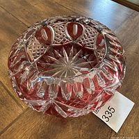Angle view of cranberry and clear crystal ashtray showing cut glass pattern and starburst design at base.