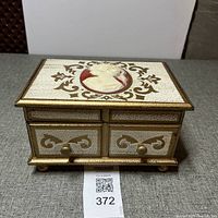 Front view of the jewelry music box showing two small drawers and gold stenciled designs with cameo inlay on top.