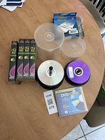 Photo showing four sealed FujiFilm HQ 160 VHS tapes, clear spindles with DVD-R and CD-R discs, a 10 pack DVD+R DL discs, and a blue box of CD/DVD sleeves.