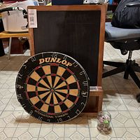 Lot with dartboard leaning against the chalkboard and jar of billiard chalk on floor showing all items together