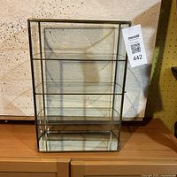 Front view showing the glass cabinet with four shelving levels, brass frame, and mirrored base.