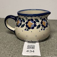 Front view of the handmade Polish pottery jug showing the blue floral design and handle.