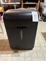 Front view of black Insignia NS-PS12CC-C shredder sitting on a tiled floor.