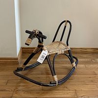 Side angle of the 1960s bamboo and rattan rocking horse showing black bamboo frame with natural rattan bindings and woven seat.